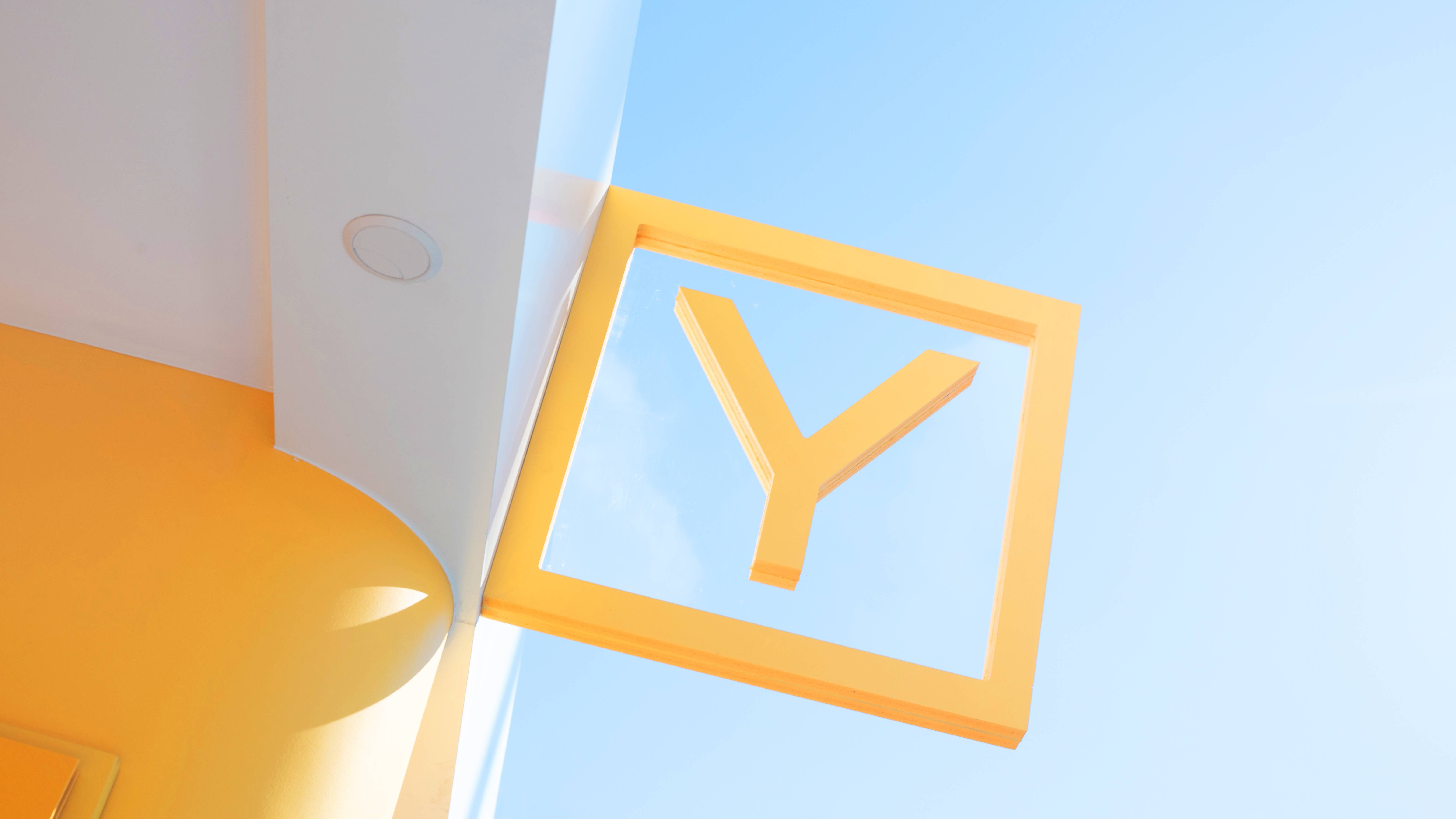 A bright yellow "Y" sign is framed by a modern architectural structure against a clear blue sky.
