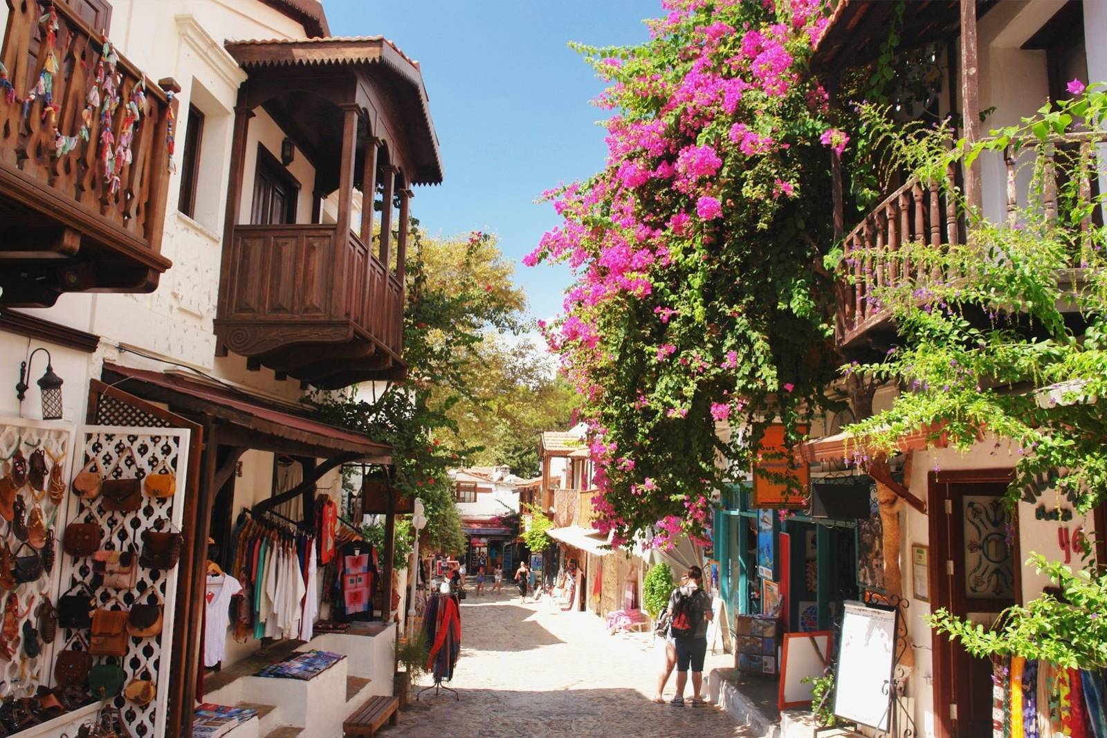 A charming cobblestone street is lined with shops and adorned with vibrant bougainvillea under a clear blue sky.