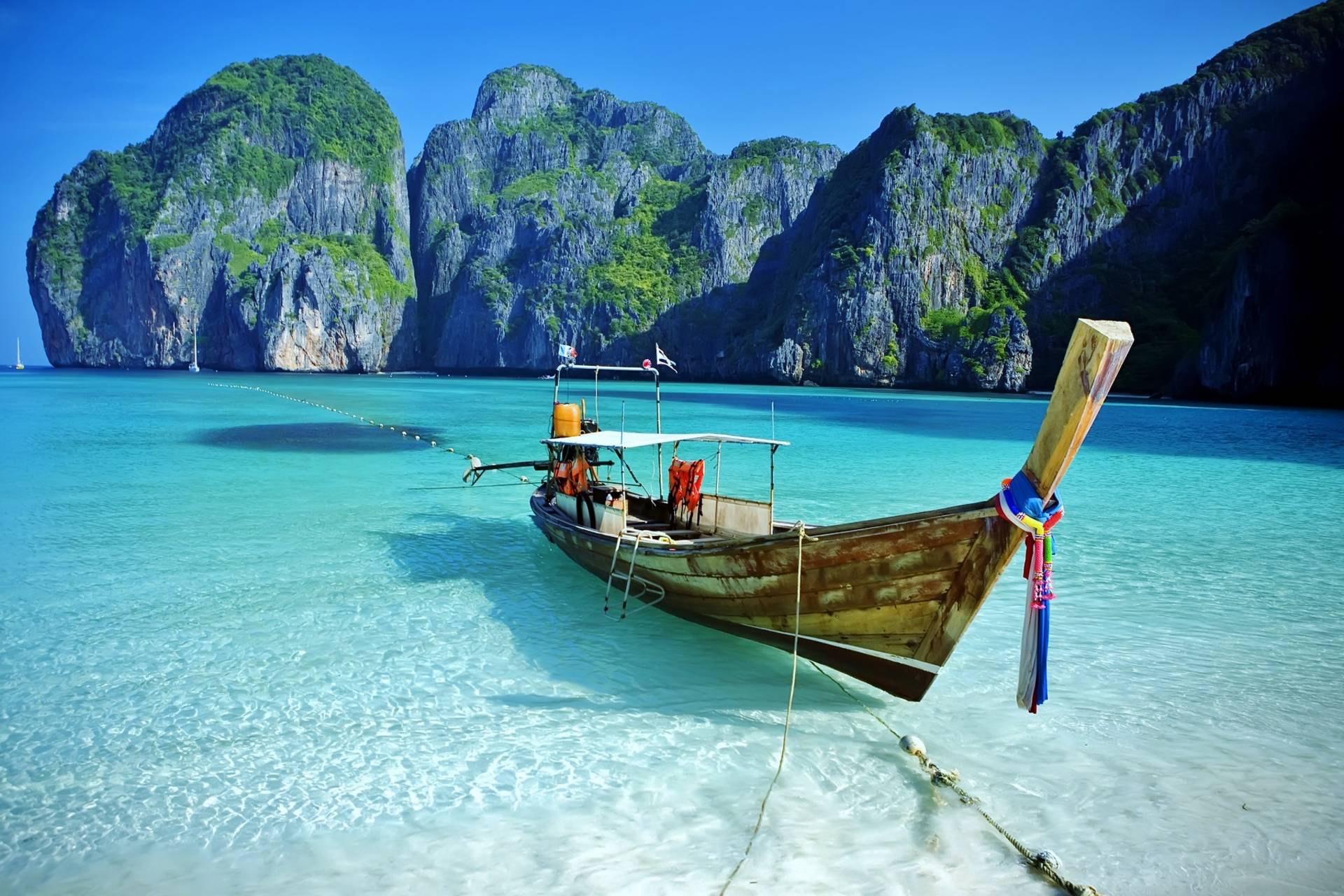 A traditional longtail boat rests in the crystal-clear turquoise waters of a tropical bay, with towering limestone cliffs rising majestically in the background.