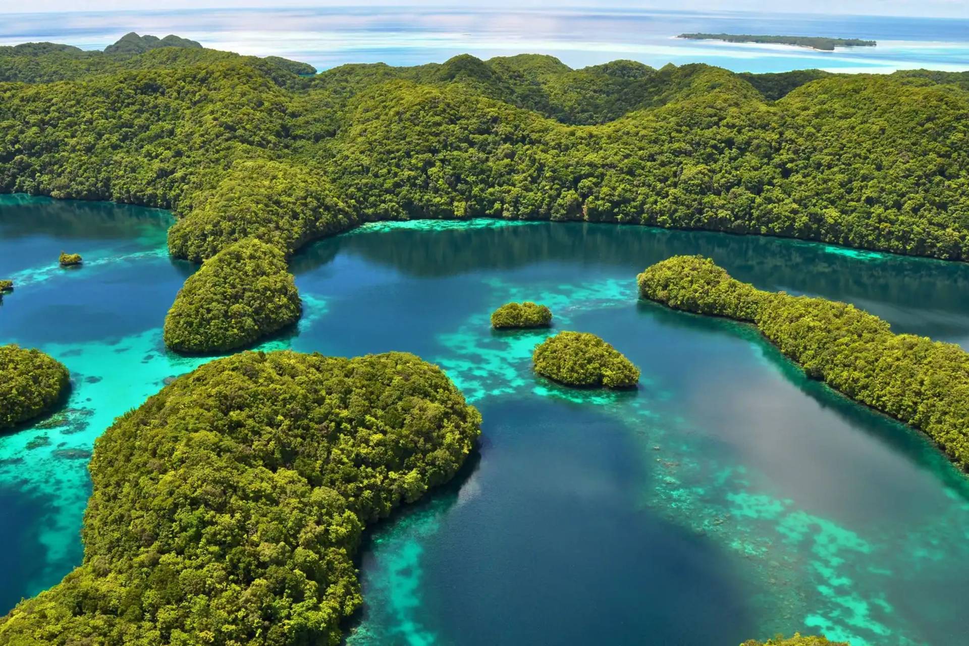 Lush green islands dot the turquoise waters of a tropical lagoon, with a distant island visible on the horizon.