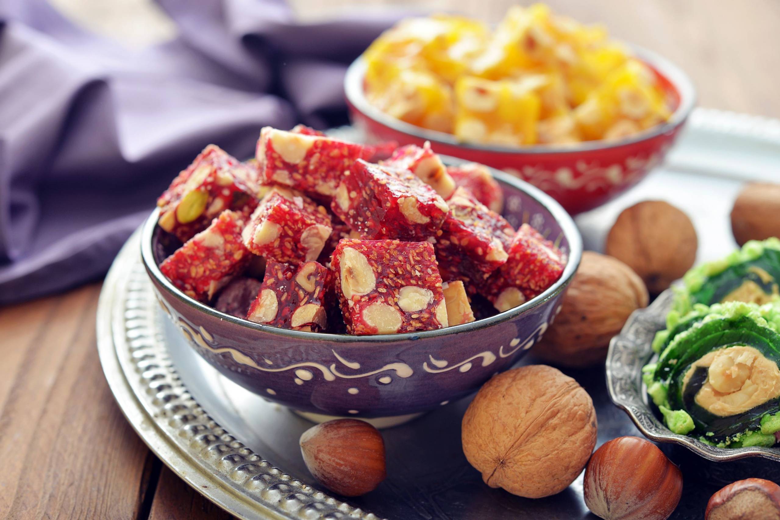 A vibrant assortment of Turkish delight and nuts are beautifully displayed on a rustic wooden table.