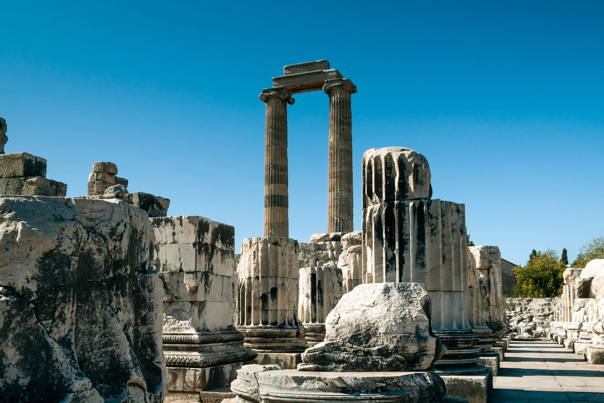 Ancient ruins of colossal stone columns stand against a clear blue sky, hinting at a glorious past.