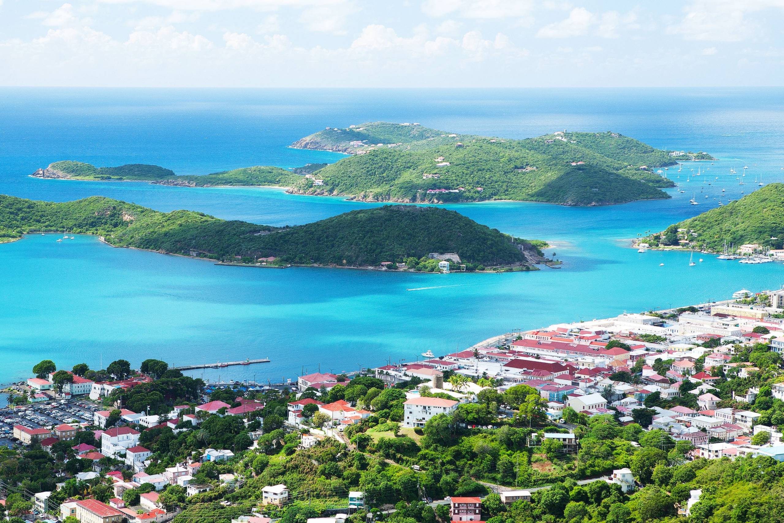 Lush green islands dot the turquoise waters of the Caribbean, with a vibrant coastal town nestled below.