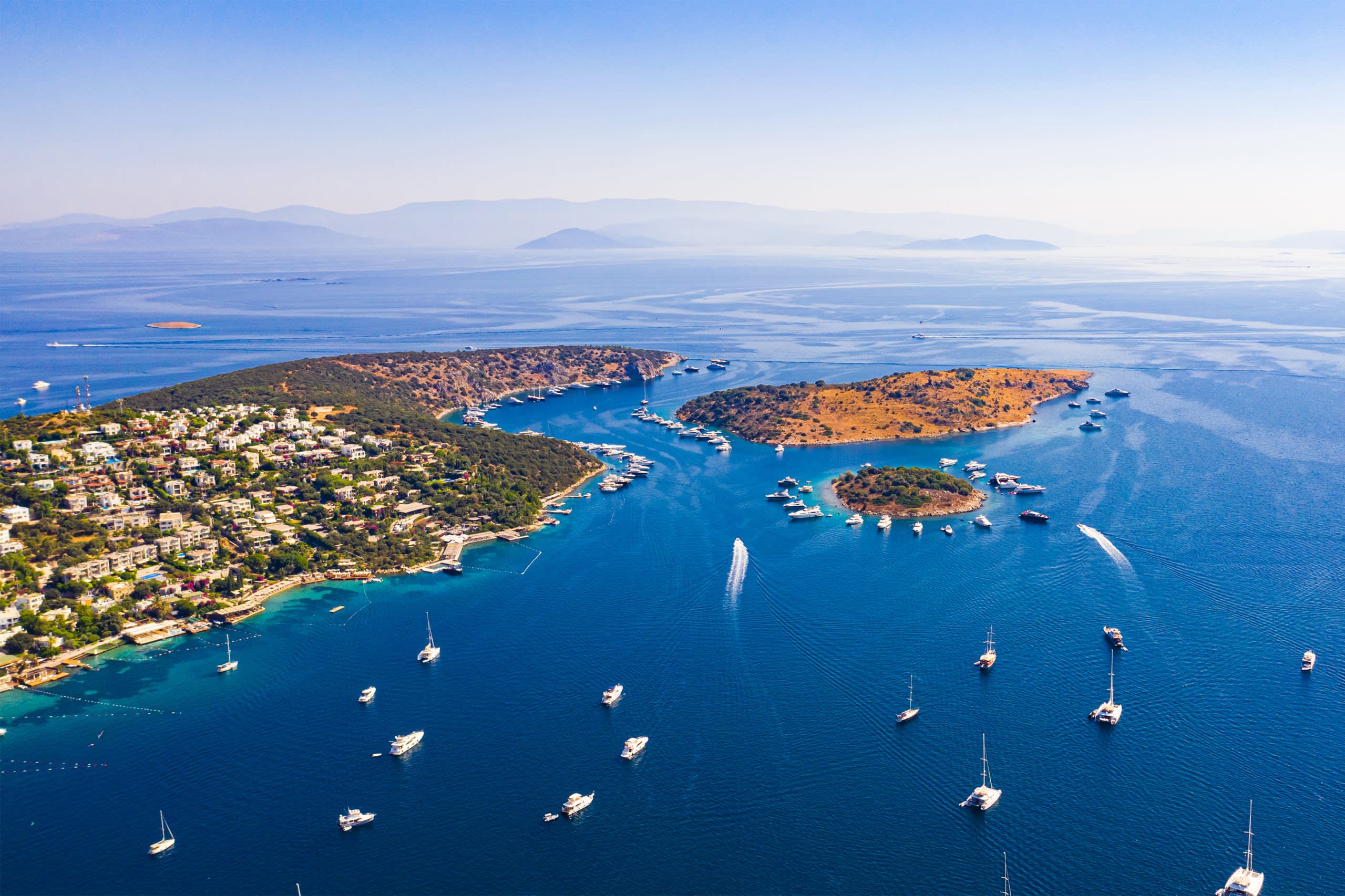 Boats dot the azure waters surrounding a lush, hillside village nestled along the Mediterranean coast.