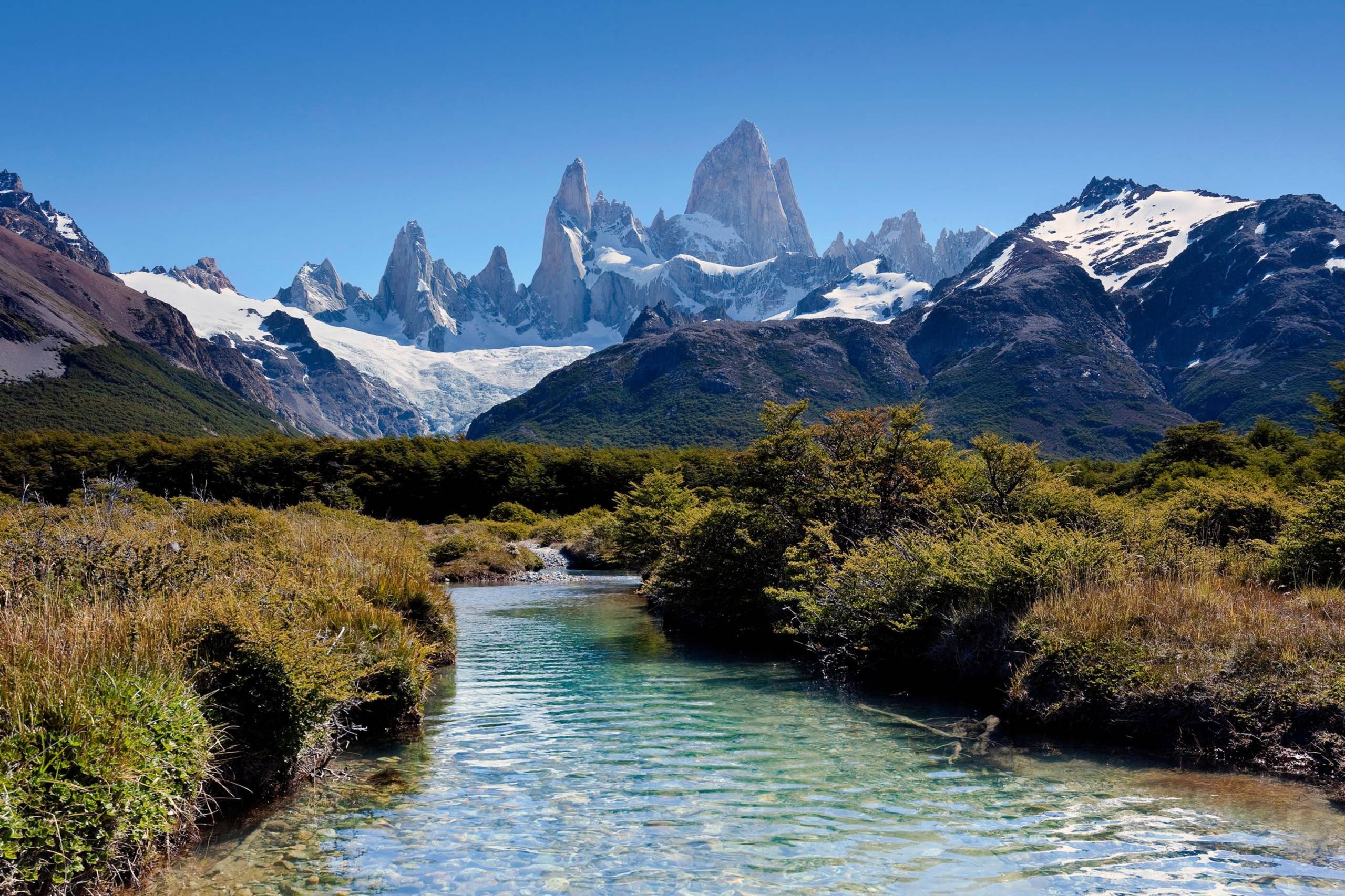 Crystal-clear waters flow through a vibrant landscape towards the majestic Fitz Roy massif in Patagonia.
