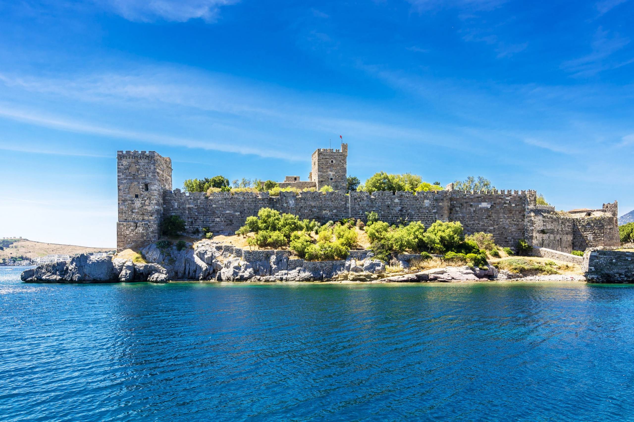 The ancient stone walls of Bodrum Castle stand majestically against a brilliant blue sky, overlooking the sparkling Aegean Sea.