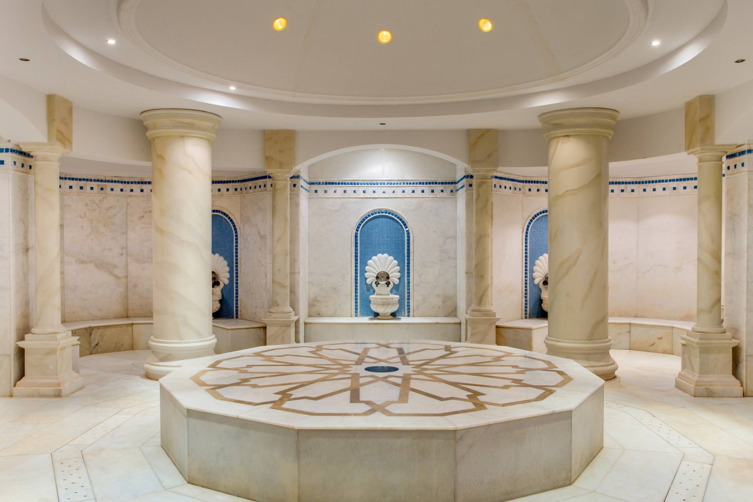 An ornate octagonal marble platform with intricate geometric patterns sits at the center of this luxurious spa's domed chamber.