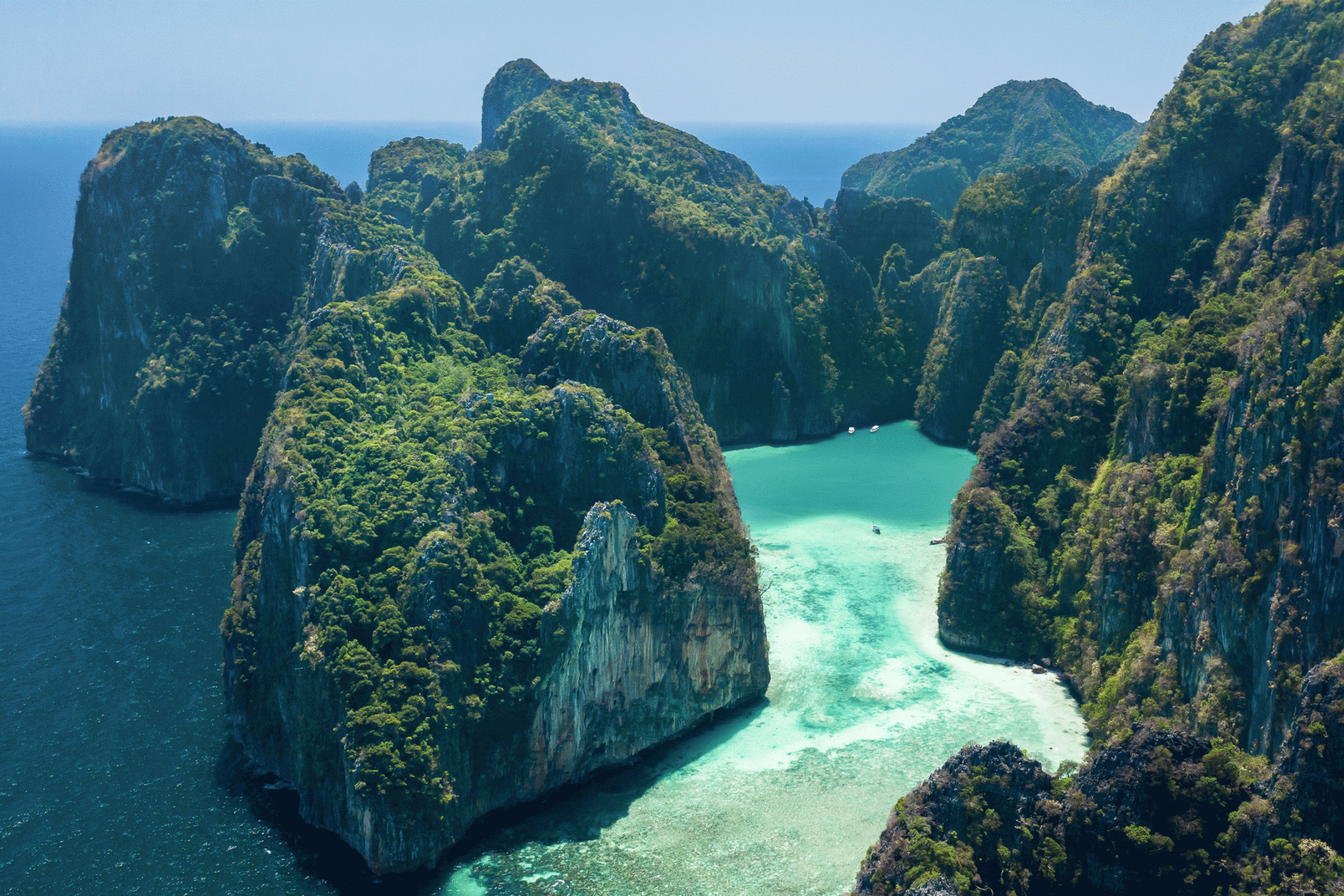 Lush green cliffs plunge into the crystal-clear turquoise waters of a secluded tropical bay.
