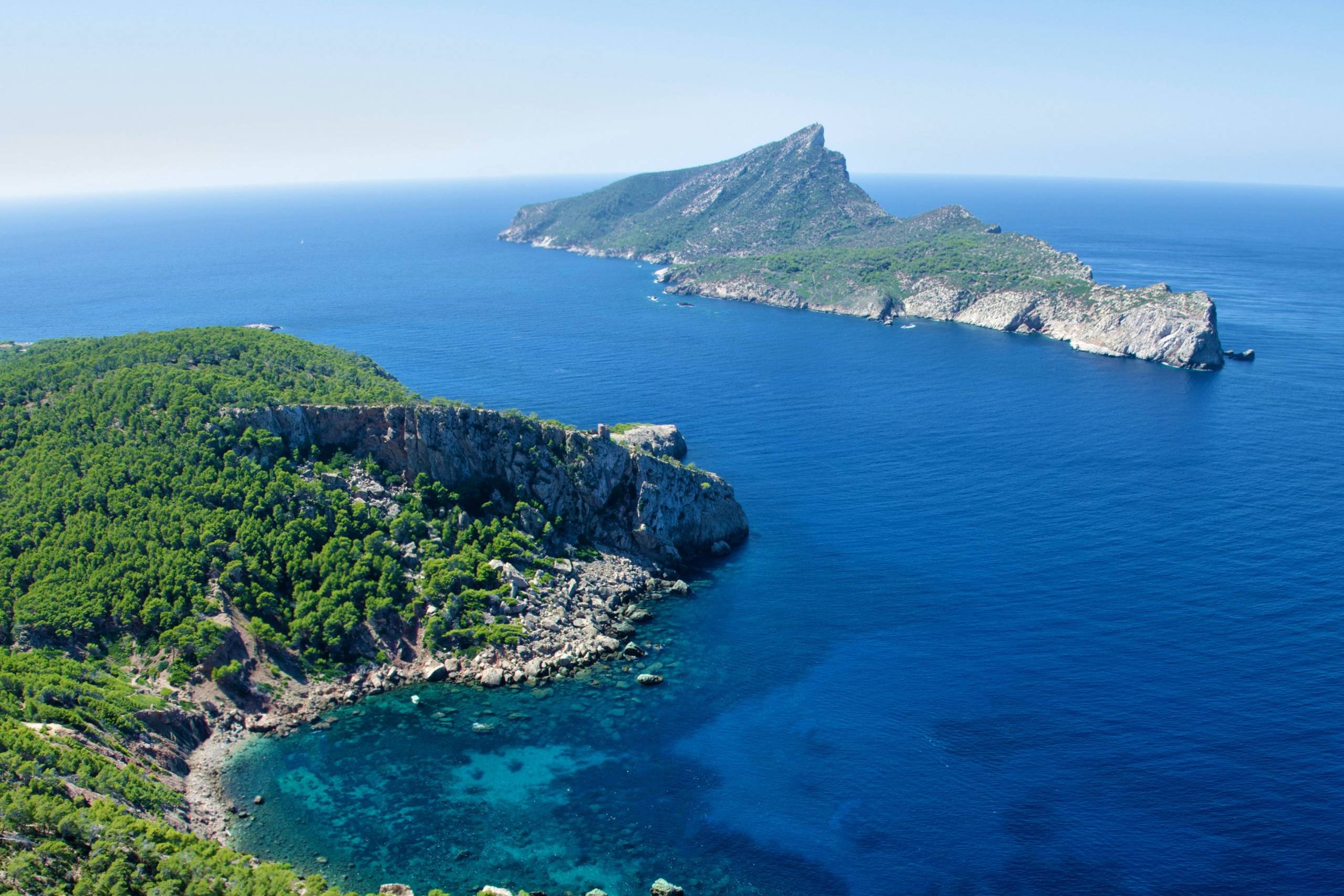 Lush green islands rise dramatically from the deep blue Mediterranean Sea under a clear sky.