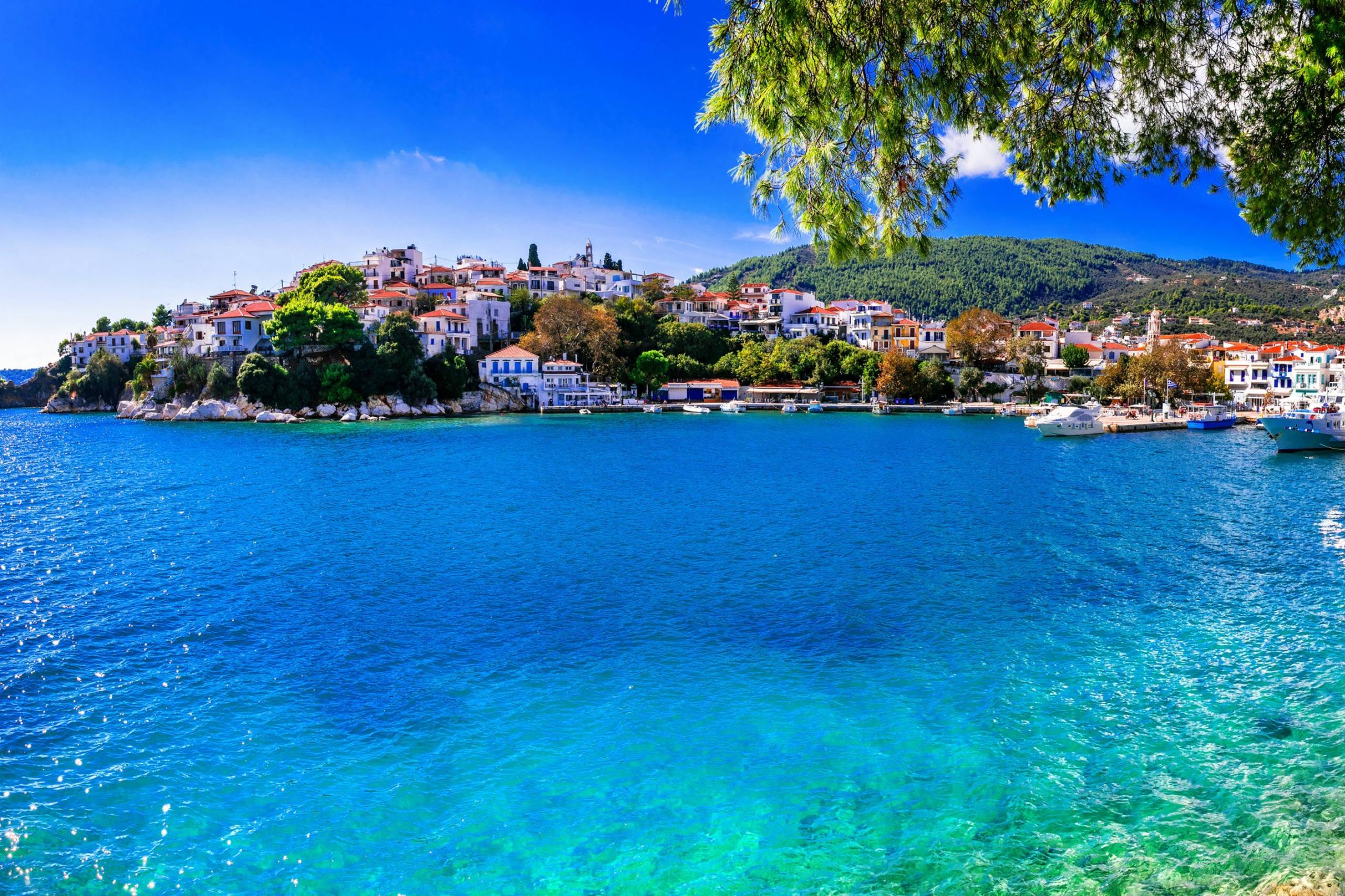 A picturesque Greek island village with white buildings and red roofs overlooks the stunning turquoise waters of the Aegean Sea.