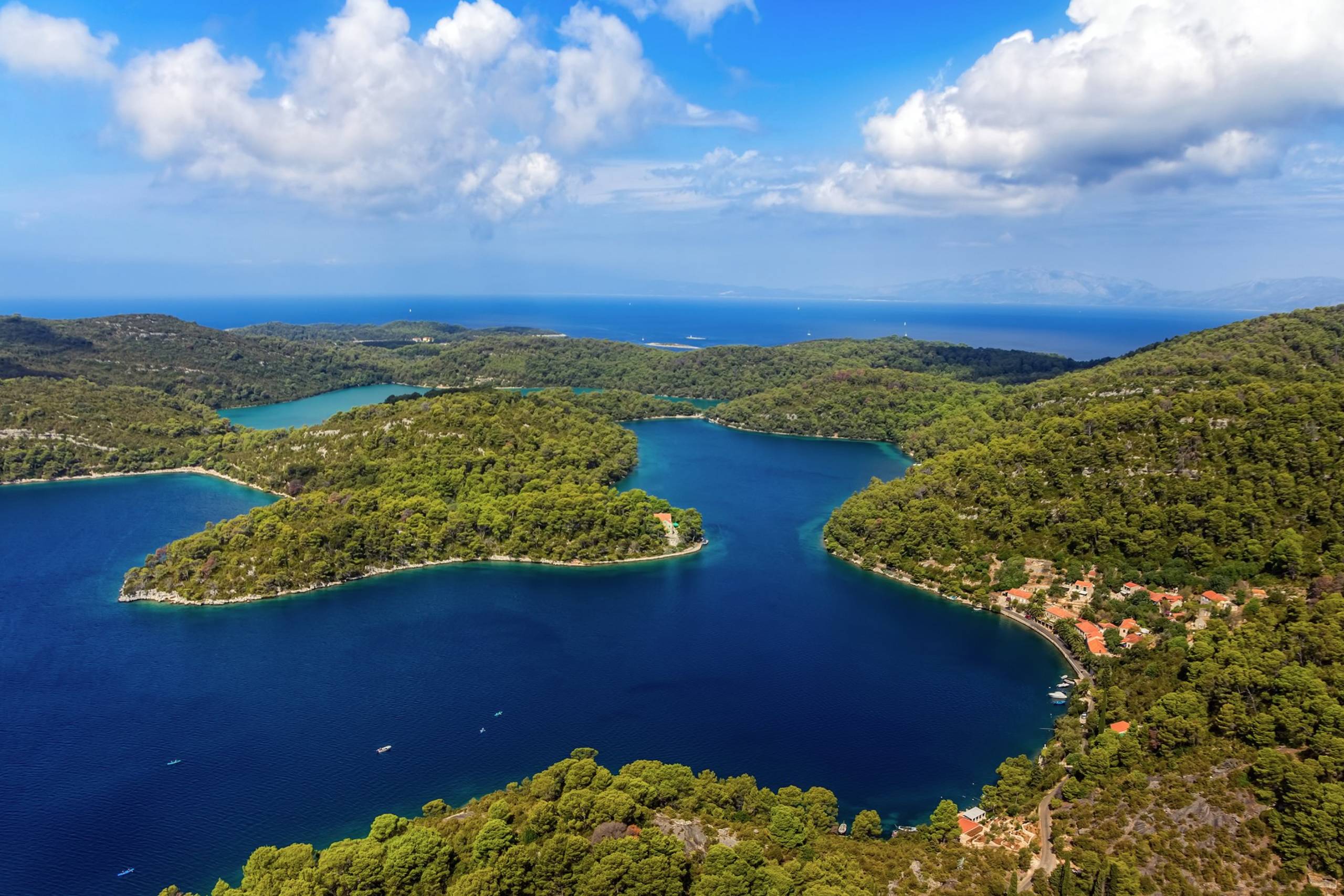 Lush green islands cradle sapphire blue waters dotted with small boats under a bright, cloudy sky.