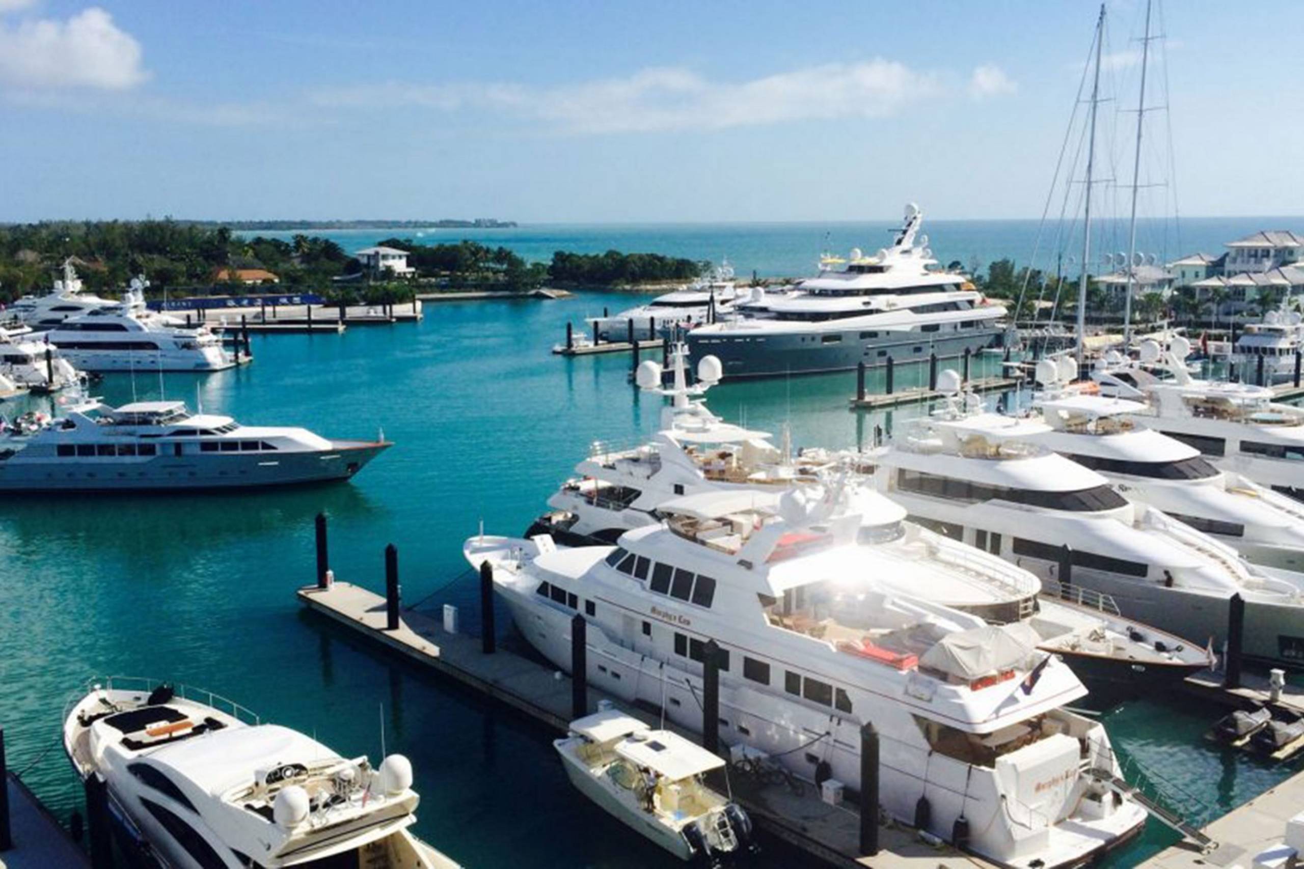 Luxurious yachts fill a pristine turquoise harbor under a bright blue sky, hinting at an opulent coastal escape.