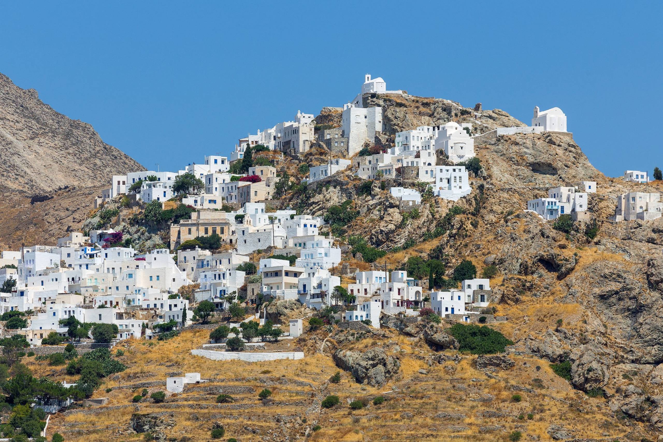 Whitewashed houses cling to a rocky hillside under a clear blue sky in this picturesque Greek village.