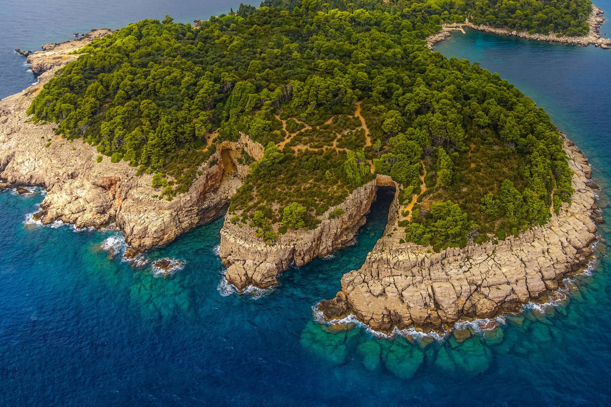 A lush green island with rugged cliffs and a dramatic sea cave meets the vibrant turquoise waters of the Adriatic Sea.