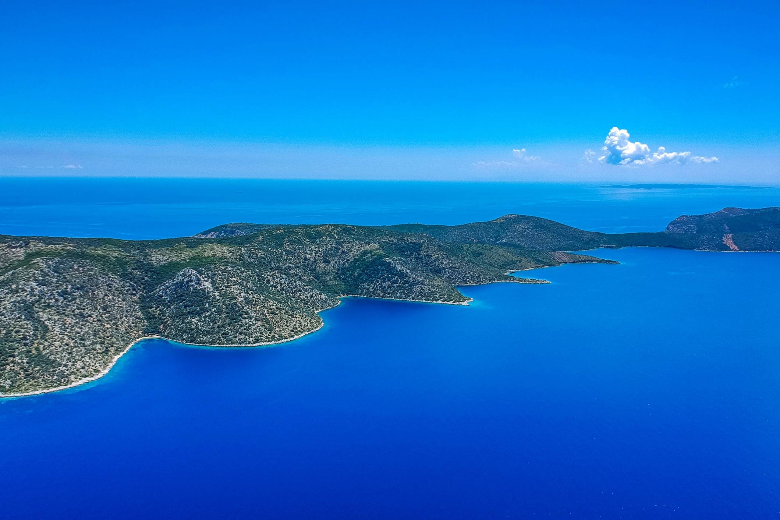 Lush green hills meet the impossibly blue waters of a secluded bay under a clear sky.