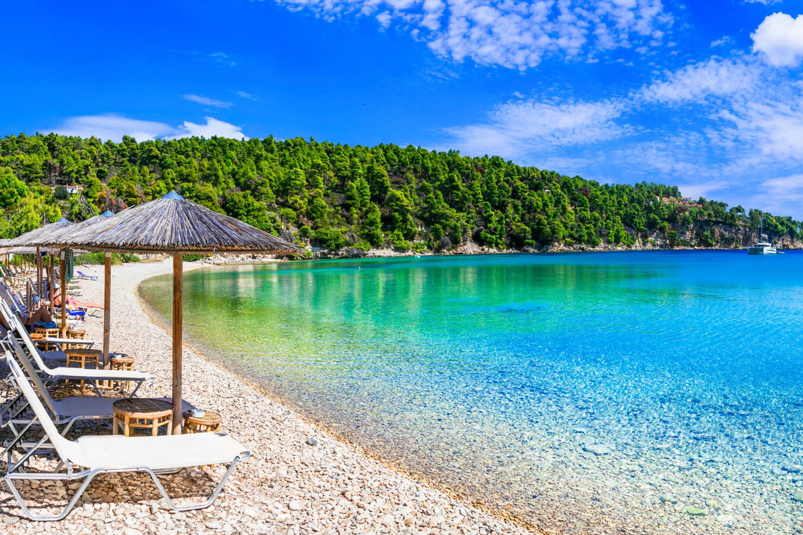 Lush green hills meet the crystal-clear turquoise waters of this idyllic pebble beach.