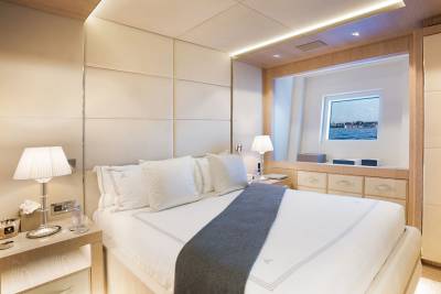 A luxurious bedroom on a yacht features a comfortable bed, elegant bedside lamps, and a window with a view of a coastal city.