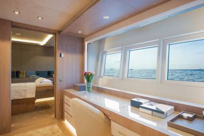 A luxurious yacht cabin offers a serene vanity area with ocean views and a glimpse into a spa-like treatment room.