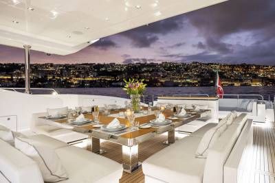 A luxurious yacht deck is set for an elegant dinner against the backdrop of a glittering city skyline at dusk.