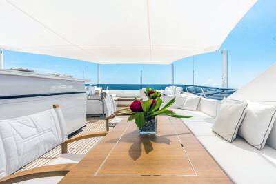 Luxurious white cushions and a floral centerpiece adorn the teak deck of this elegant yacht under a bright blue sky.
