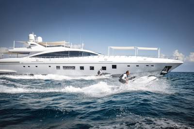 Two jet skiers race alongside a luxurious white yacht under a clear blue sky.