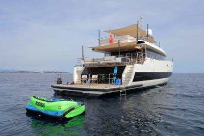 A vibrant inflatable tube bobs in the calm blue water beside a sleek white yacht ready for aquatic adventures.
