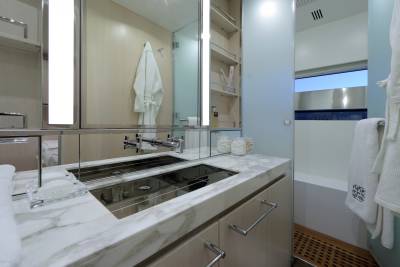 A luxurious bathroom features a marble countertop, sleek chrome fixtures, and plush white robes hanging beside a bathtub.