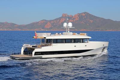 The sleek white yacht "Alexandra" cruises through the azure waters with rugged, red-hued mountains in the background.