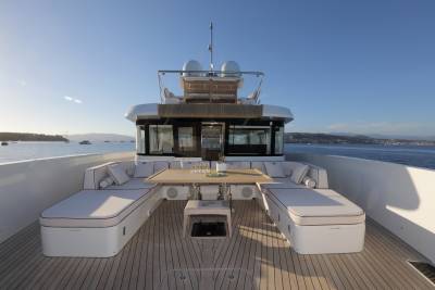 A luxurious yacht deck offers a comfortable seating area with a table set for drinks and snacks, overlooking a serene bay.