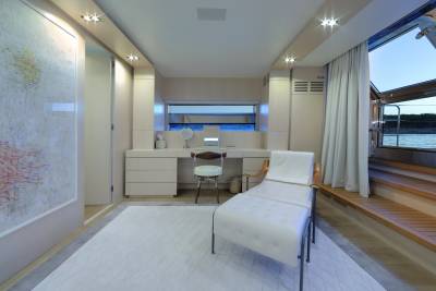 A luxurious yacht cabin features a vanity, a chaise lounge, and a large window overlooking the water.