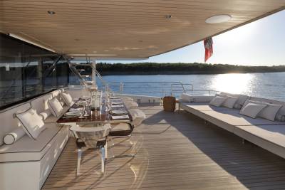 A beautifully set dining table awaits guests on a sun-drenched yacht deck overlooking a tranquil sea.