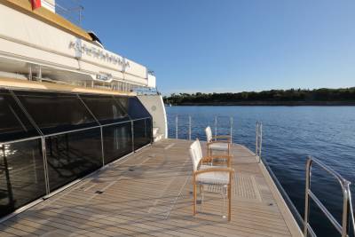 Two white chairs with wooden frames sit on the teak deck of a luxury yacht overlooking a calm blue sea.