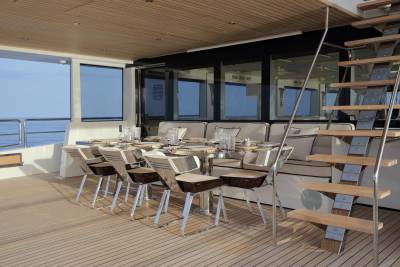 An elegant outdoor dining area on a yacht features a polished table, modern chairs, and a sleek staircase leading to another deck.