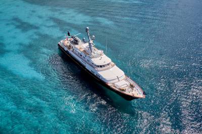 A luxurious yacht with a helicopter and jet skis glides through crystal-clear turquoise waters.
