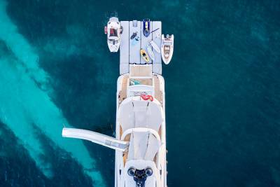 An aerial view captures a luxury yacht adorned with a slide and various watercraft docked in crystal-clear turquoise waters.