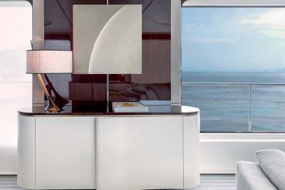 A stylish white credenza with a modern lamp and art piece sits beside a large window overlooking the serene ocean.
