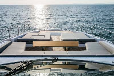Relax on the spacious deck of this luxury yacht, with plush seating and a wooden table overlooking the shimmering ocean.