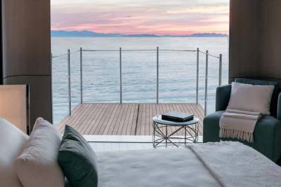 A serene bedroom opens onto a tranquil sea view with a colorful sunset painting the horizon.