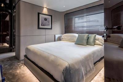 A luxurious bedroom on a yacht features a plush bed with soft pillows and a fringed throw, complemented by minimalist decor and ambient lighting.
