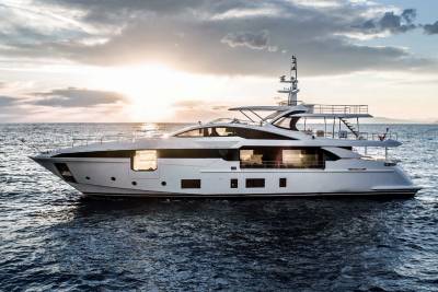 A sleek white yacht glides across the calm sea under a dramatic sunset sky.