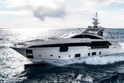 A sleek white yacht cuts through the choppy blue ocean under a bright, cloudy sky.