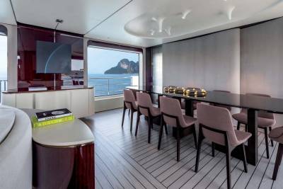 A modern dining area on a yacht offers a stunning view of a tropical island through a large panoramic window.