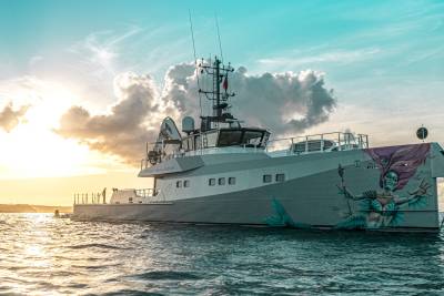 A striking mermaid mural adorns the stern of the Pink Shadow yacht as it sails through the tranquil ocean at sunset.