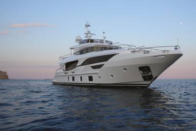 A luxurious white yacht glides across calm blue waters under a soft twilight sky with a distant castle.