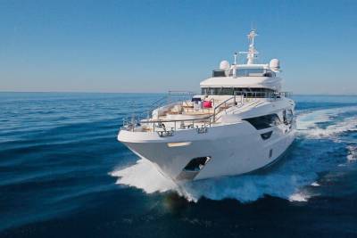 A sleek white yacht cuts through the deep blue ocean under a clear sky.