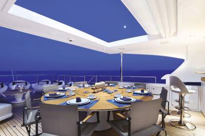 An elegant yacht deck dining area is set for a meal under the twilight sky with a modern bar nearby.