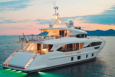 A luxurious white yacht with illuminated steps and underwater lights rests on calm turquoise waters at sunset.