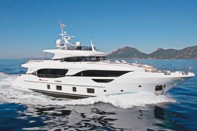 A sleek white yacht cruises through the sparkling blue ocean with mountainous islands in the background.