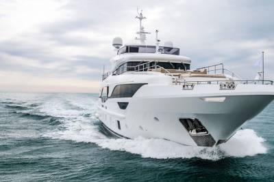 A sleek white yacht cuts through the choppy blue water under a cloudy sky.
