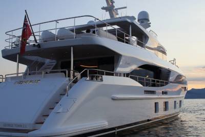 A luxurious white yacht named "Aqualler" sails on calm waters at sunset with mountains in the background.